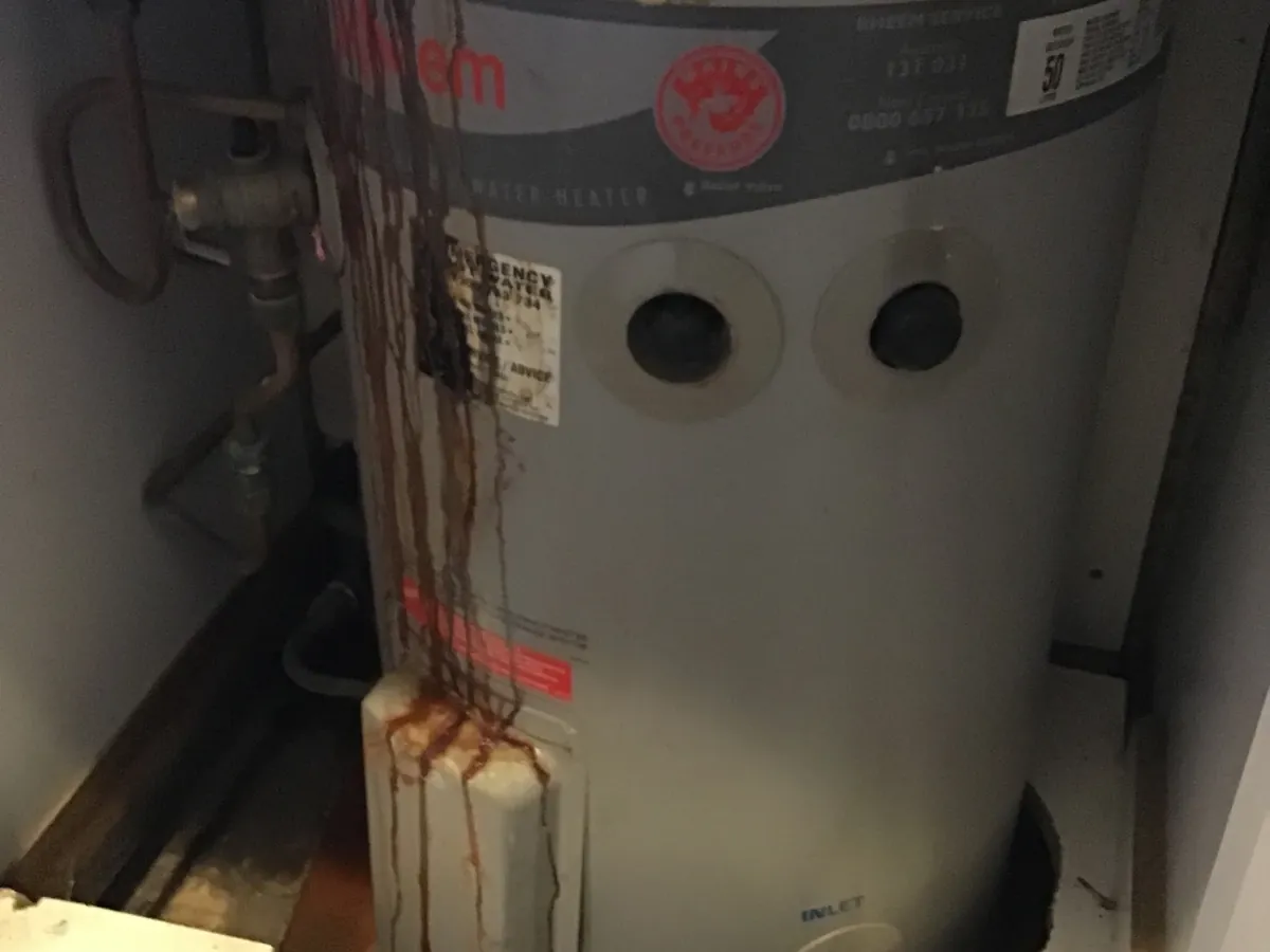 Rust and water marks running down an old electric hot water tank onto its tray in Ashfield