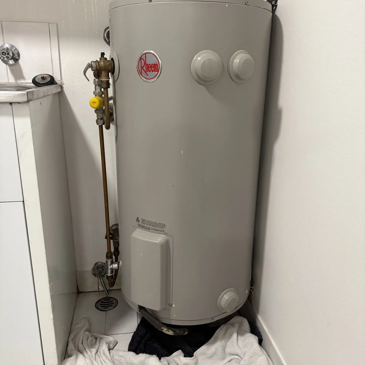 Rheem electric hot water tank with towels on the floor underneath it in a laundry in Redfern