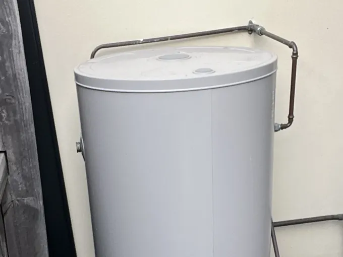Grey electric hot water tank on a paver between a timber fence and a rendered wall in Macquarie Fields
