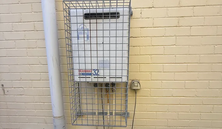Continuous flow gas hot water unit in a wire cage on a brick wall in Oatley