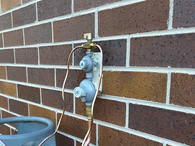 Changeover regulator and copper gas lines on an LPG supply against a brick wall in Berowra Heights