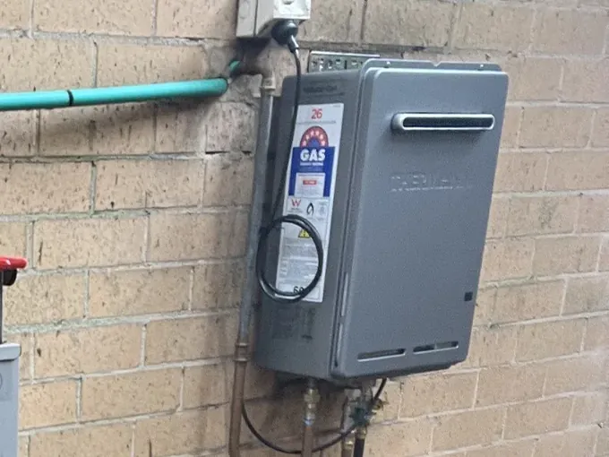 Gas appliance connected to its copper gas line and isolation valves on a brick wall in Cremorne