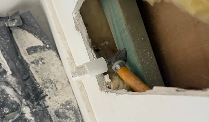 Plasterboard cut open to reach a capped gas fitting and orange gas pipe inside the wall in Carramar