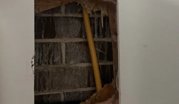Yellow gas pipe exposed through an opening cut in a plasterboard wall in Casula