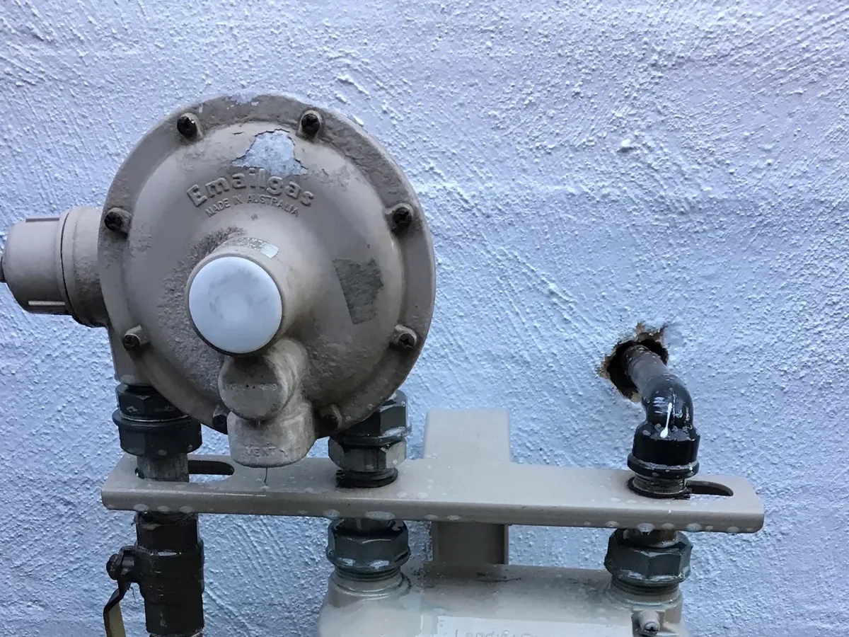 Gas regulator, valves and pipework above a gas meter on a painted wall in Kellyville