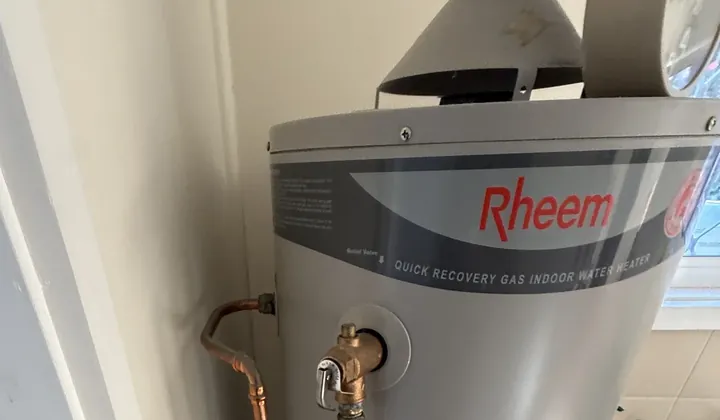 Indoor gas storage hot water unit with a flue hood on top and copper pipes in Tempe