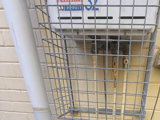 Old continuous flow gas unit behind a wire cage with its worn pipes below it in Oatley