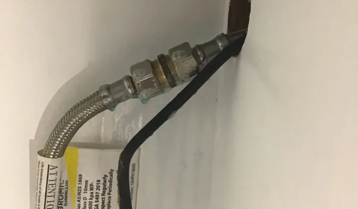 Braided gas hose joined to an older gas line in an appliance cupboard, with blue leak test fluid on it, in Pendle Hill