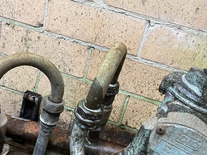 Old corroded gas pipework and regulator against a brick wall in Cremorne