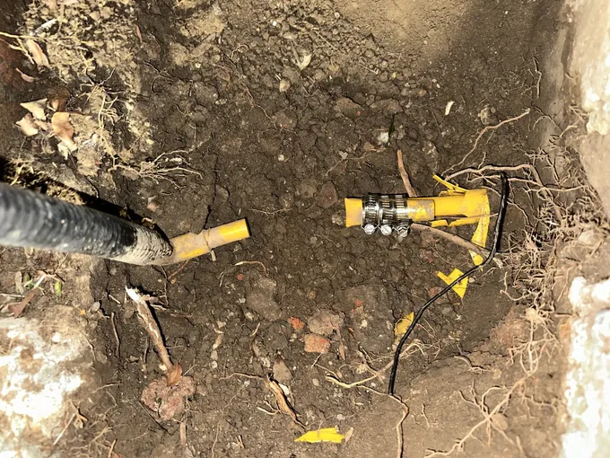 Yellow gas service pipe exposed in a dug hole at night, with a stainless repair coupling clamped on, in Earlwood