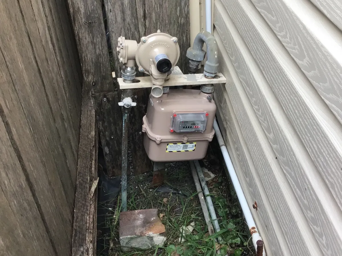 Gas meter and regulator in a narrow side passage between a timber fence and a house in Tempe