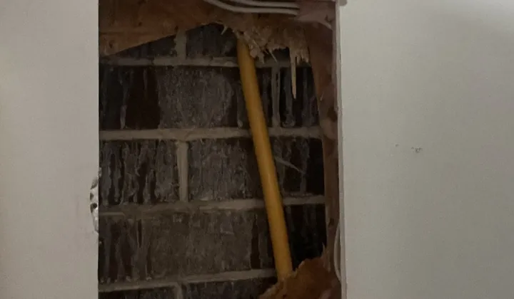 Yellow gas pipe inside a wall cavity, seen through an access hole cut in the plasterboard in Casula