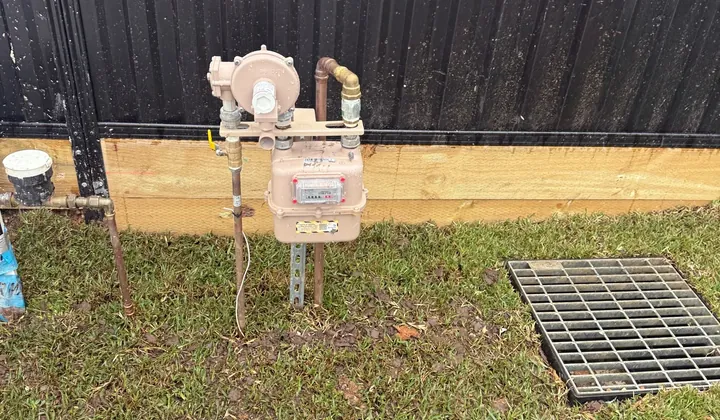 Gas meter and regulator on a steel stand with copper pipework beside a black fence in Carramar