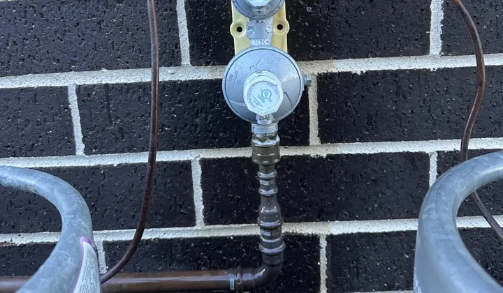 Twin LPG bottle regulator with copper gas pipe on a dark brick wall in Condell Park