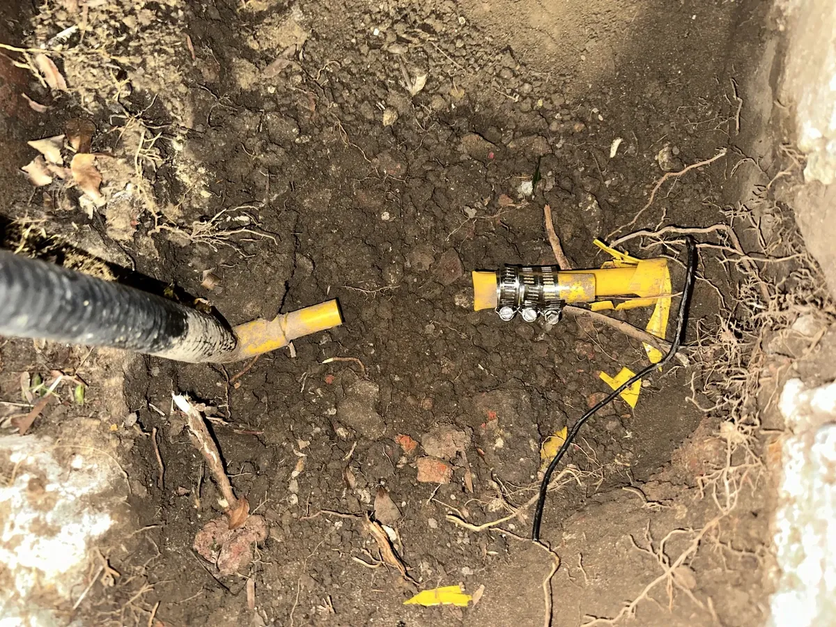 Broken yellow gas pipe with hose clamps exposed in a dug hole in Earlwood