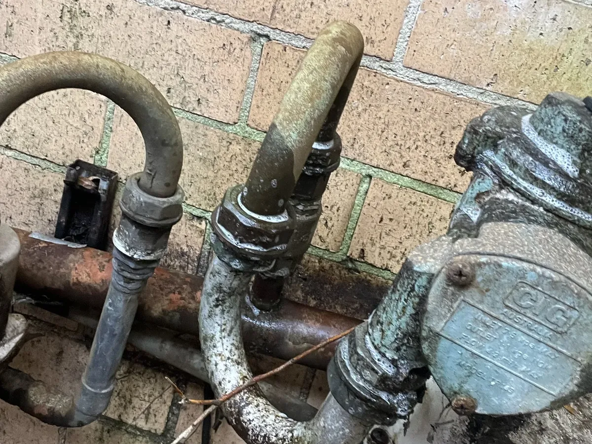 Old galvanised gas pipework and a worn regulator on a brick wall in Cremorne