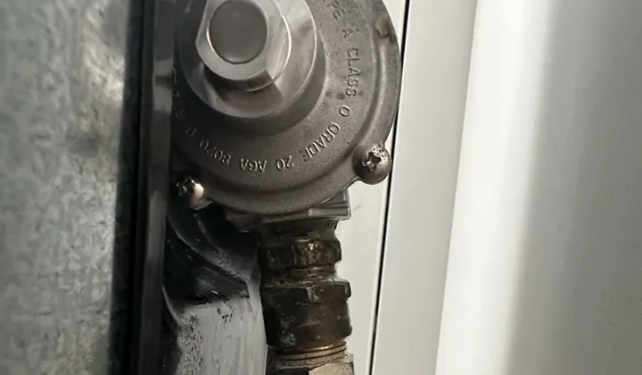 Gas regulator and brass fittings on the back panel of a freestanding stove in Collaroy