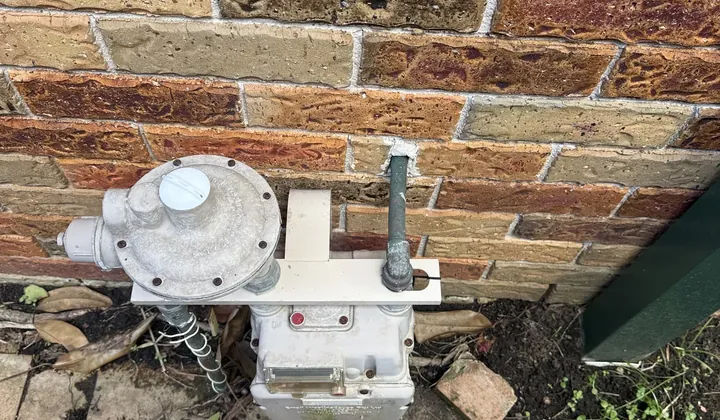 Gas meter and regulator on a brick wall beside a paved path