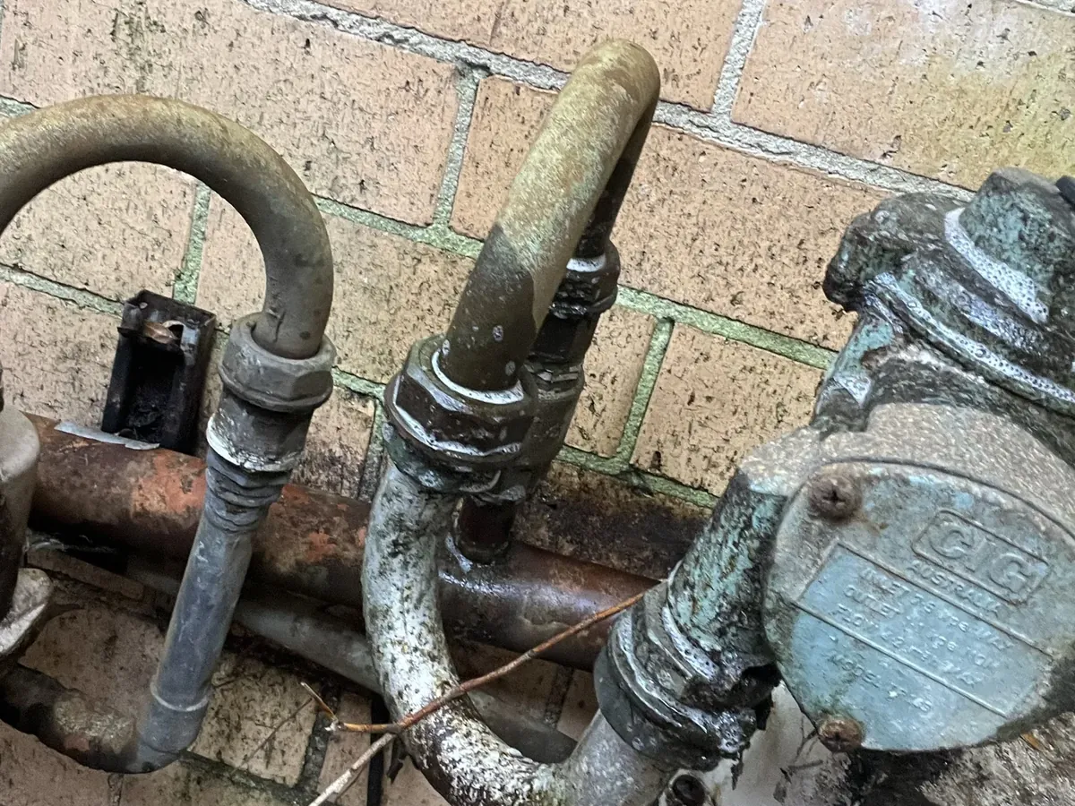 Old corroded gas pipework beside a gas meter on a brick wall