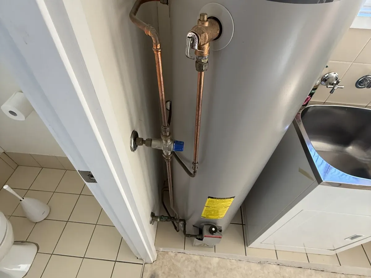 Rheem indoor gas storage hot water system in a laundry with its relief valve and copper pipework