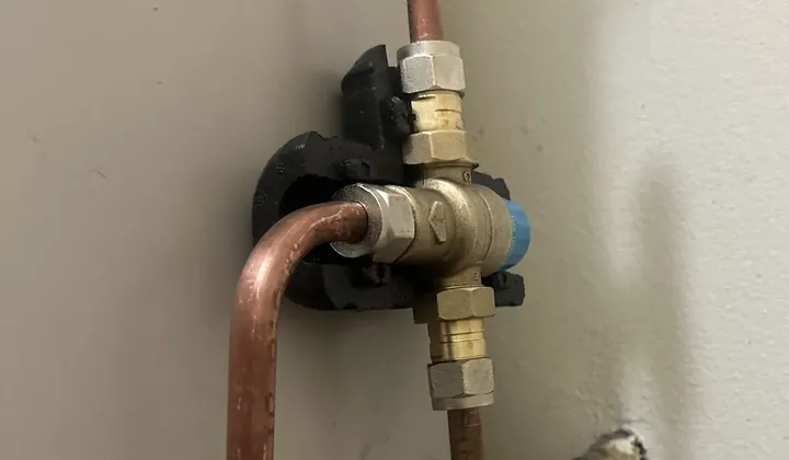 Tempering valve with copper pipework fixed to the side of a hot water tank in Bankstown