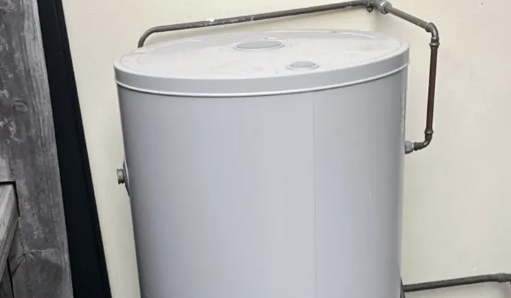 Grey electric hot water tank on a paver between a timber fence and a rendered wall in Macquarie Fields