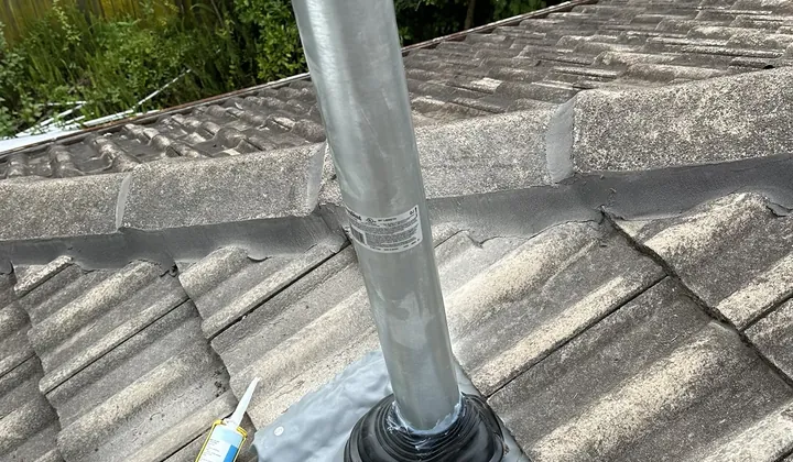 New flue pipe coming up through roof tiles with fresh flashing and a sealant gun beside it in South Turramurra
