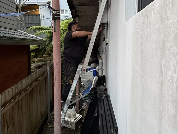 Mr Splash plumber up a ladder working on the wall unit down the side of a Beacon Hill home