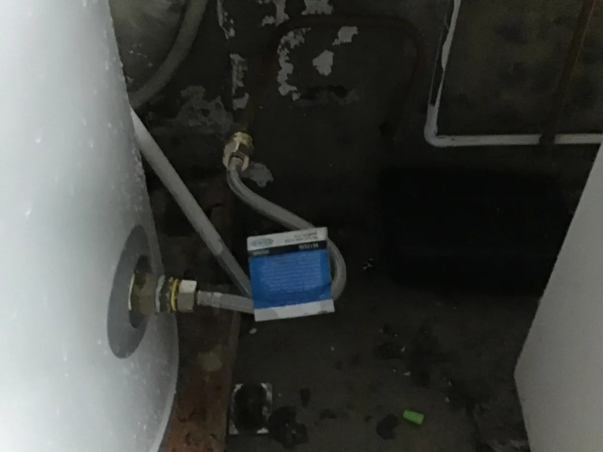 Old hot water tank and its flexible water connection in a dark Surry Hills laundry