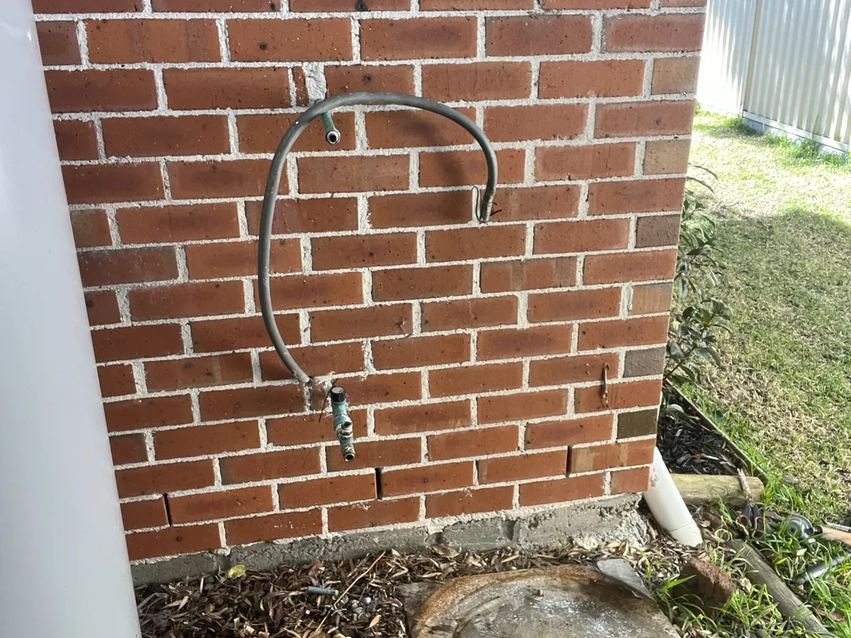 Braided water connection on the brick wall beside an old electric hot water tank in Caringbah South
