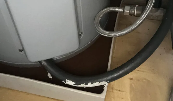 Base of an electric hot water tank standing in a leak tray with its braided water connection in Randwick