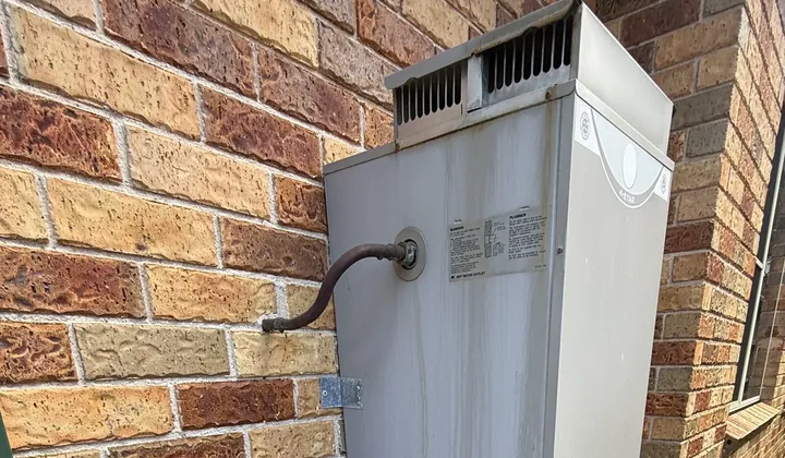 Old gas storage hot water unit with its flue cowl against a brick wall in Allambie Heights