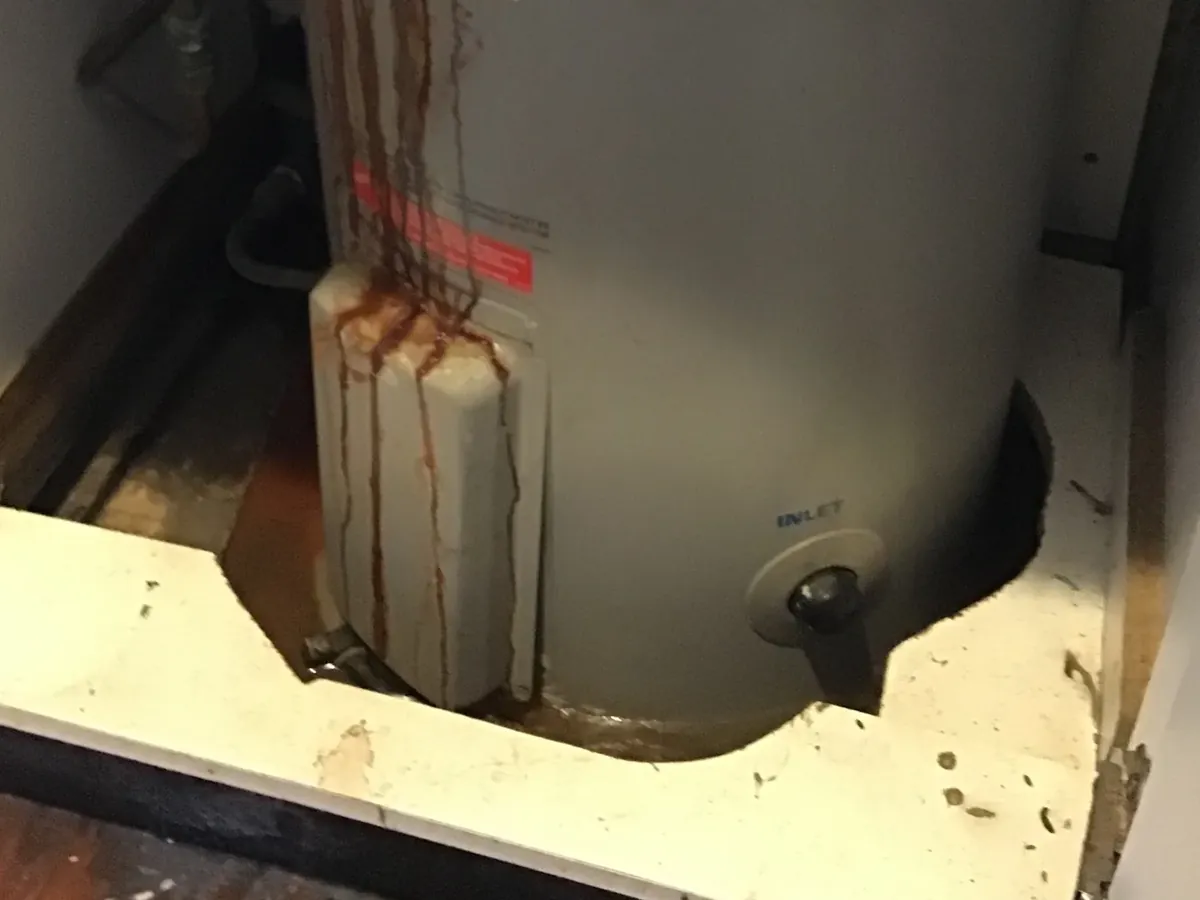 Rust and water marks running down an old electric hot water tank onto its tray in Ashfield
