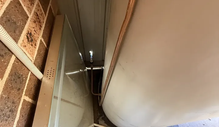 Water pooled on the concrete beside a hot water tank in a narrow space