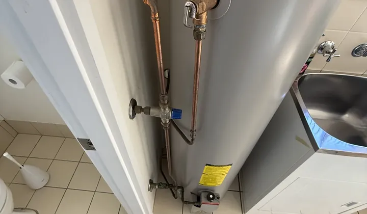 Rheem indoor gas storage hot water system with its relief valve and pipework in a laundry