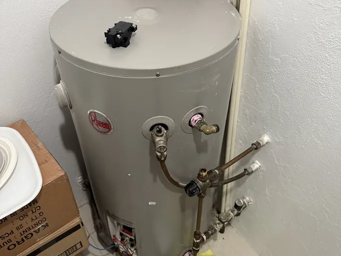 Electric hot water tank with its cover off and tools on the floor during a check