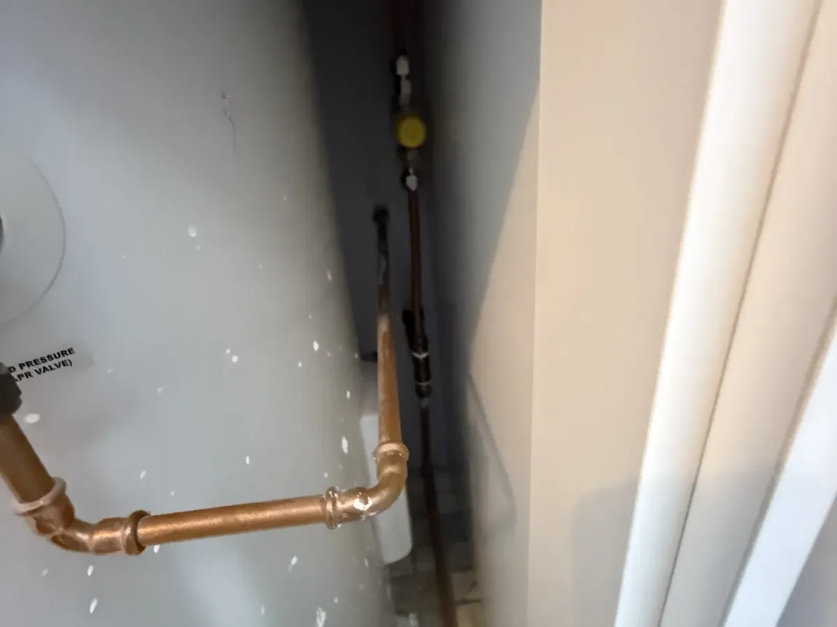 Hot water tank in a tight cupboard with water marks on its side and copper pipework