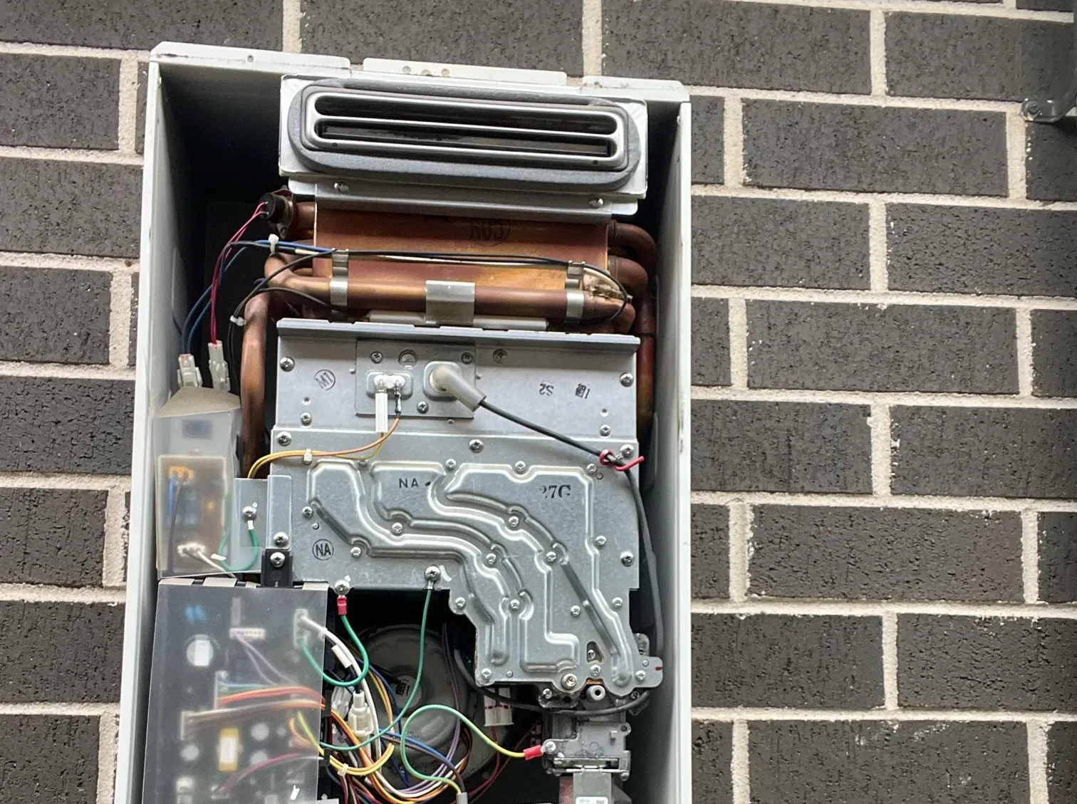 Continuous flow gas hot water unit opened up with its front cover off on a dark brick wall in Oran Park