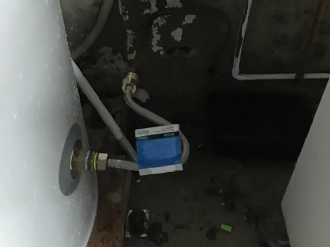 Old hot water tank and its flexible water connection in a dark Surry Hills laundry