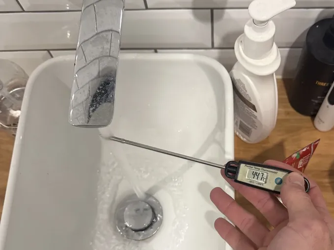 Thermometer held under a running bathroom basin tap to check the hot water temperature in Tamarama