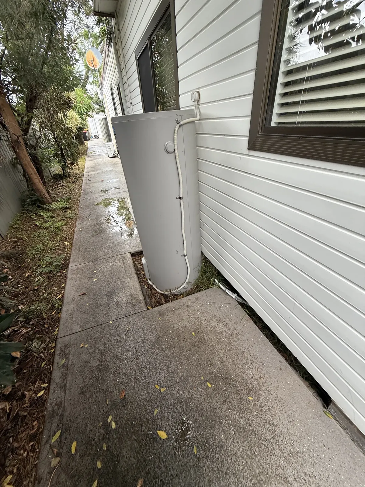 Electric storage hot water system beside a weatherboard house