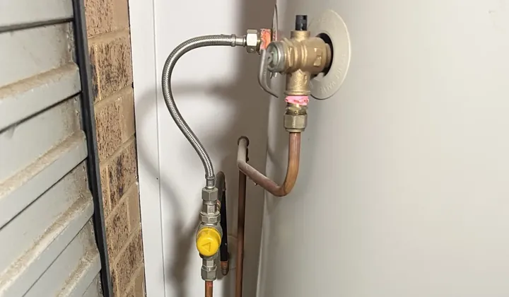 Brass valve, braided hose and yellow isolation valve on top of an electric tank beside a roller door in Illawong