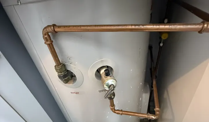 Relief valve and copper pipes on the side of a storage tank inside a cupboard in Bexley