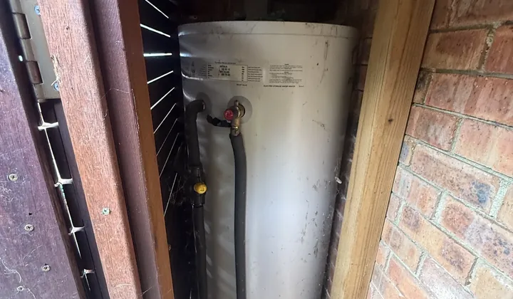 Electric hot water tank inside a timber enclosure against a brick wall in Cremorne