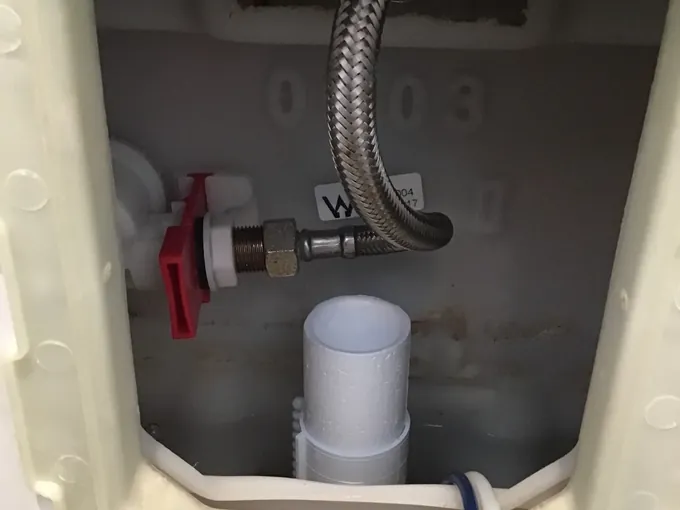 In-wall cistern opened through the flush plate panel showing the stop tap and inlet hose