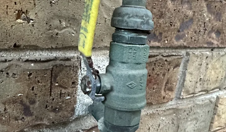 Yellow-handled gas isolation valve on an old gas pipe against a brick wall in Rouse Hill