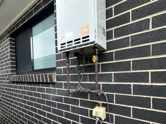 Continuous flow gas hot water unit connected on a brick wall with its gas line and controller in Austral