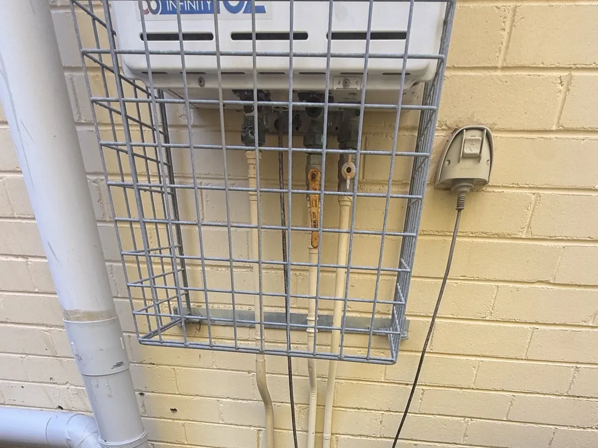 Continuous flow gas hot water unit behind a wire cage on an outside wall in Oatley