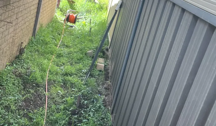 Orange hose reel at the end of a grassy side passage on a blocked outdoor drains job in Rosemeadow