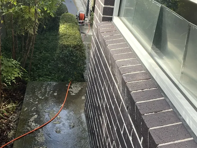 Jet hose from a hose reel run along a wet side path strewn with muck in Hunters Hill